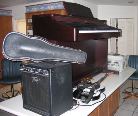 A piano, a bass guitar, an amplifier, and a violin share space on a countertop, away from water